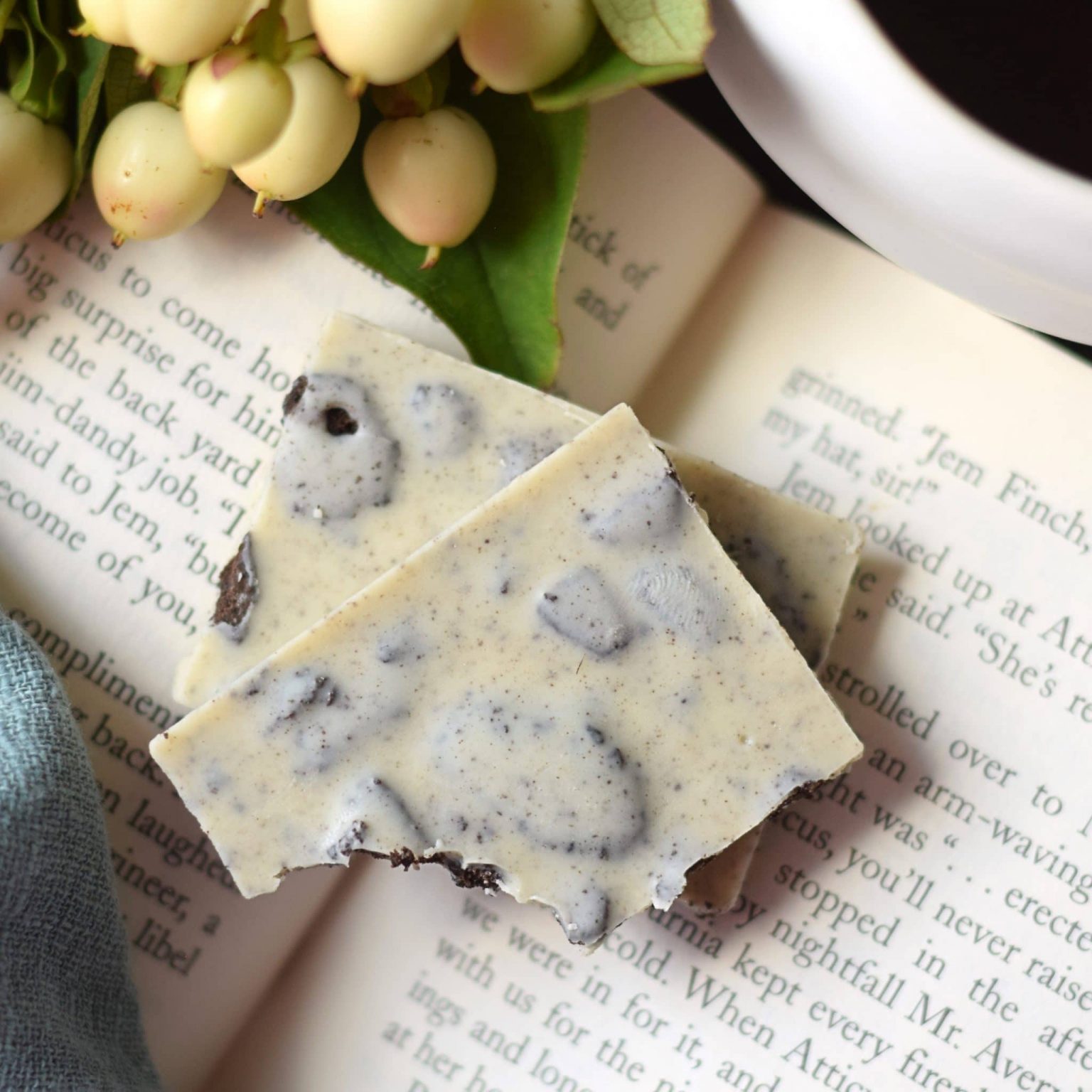 2 pieces of a white chocolate artisan bar with pieces of Oreos in it; pieces are sitting on an open book