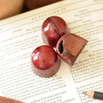 3 red gourmet chocolate truffles sitting on an open book; one truffle is cut in half and has ganache inside and balsamic vinegar spilling out