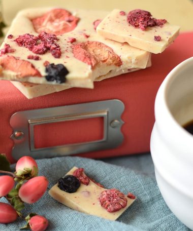 Pieces of a gourmet white chocolate artisan bar embedded with dried raspberries, blueberries, and strawberries sitting on a pink book with a metal label holder on the spine