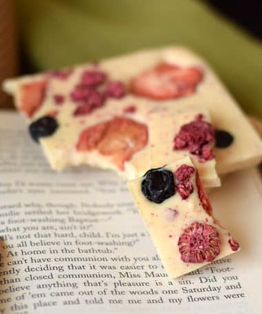 Two pieces of a gourmet white chocolate bar embedded with berries sitting on top of an open book
