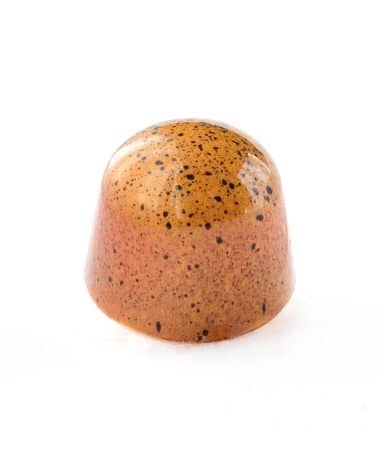 Side view of a light orange-red gourmet chocolate truffle specked wit black specks; truffle tastes like passion fruit