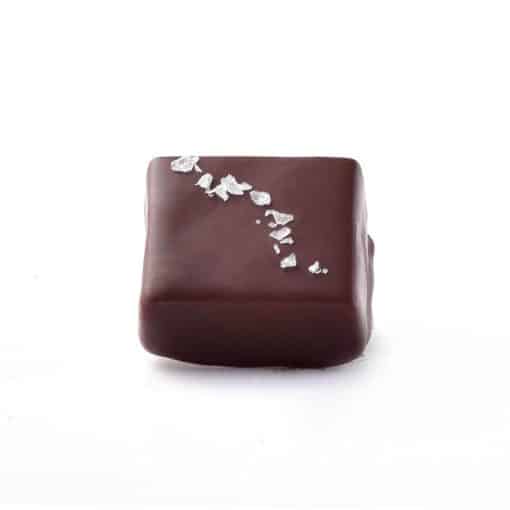 Side view of a gourmet dark chocolate truffle that is sprinkled with sea salt; truffle tastes like sea salt caramel