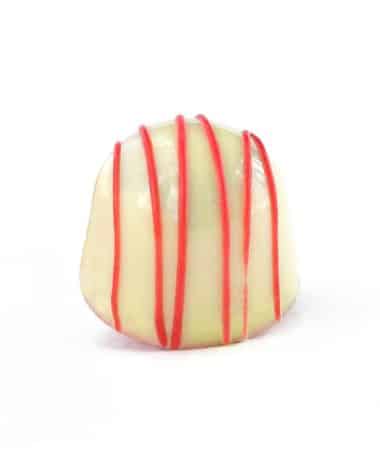 Side view of a cream colored gourmet chocolate truffle with red stripes; truffle tastes like white chocolate raspberry