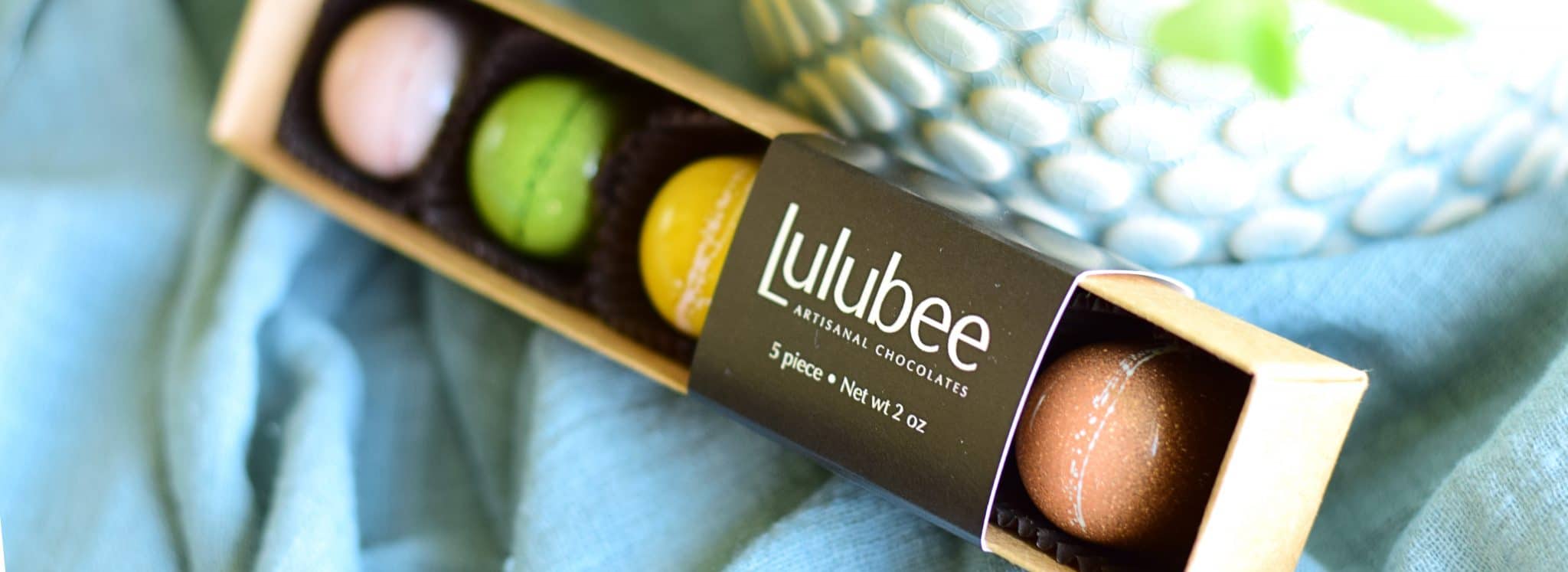 5 gourmet chocolate truffles in pastel colors in a box that has a cigar band that reads Lulubee Artisanal Chocolates