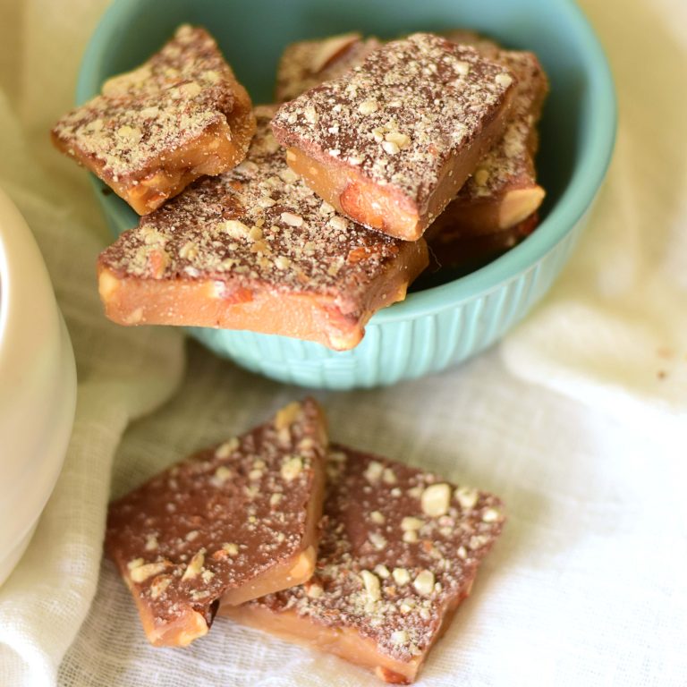 Bowl filled with pieces of English toffee with gourmet milk chocolate spread on top and then sprinkled with chopped almonds