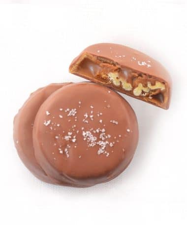 Overhead view of three gourmet Milk Chocolate Pecan Turtles; one turtle is cut in half to reveal the caramel and pecans inside