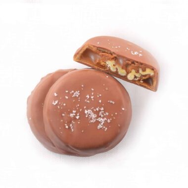 Overhead view of three gourmet Milk Chocolate Pecan Turtles; one turtle is cut in half to reveal the caramel and pecans inside