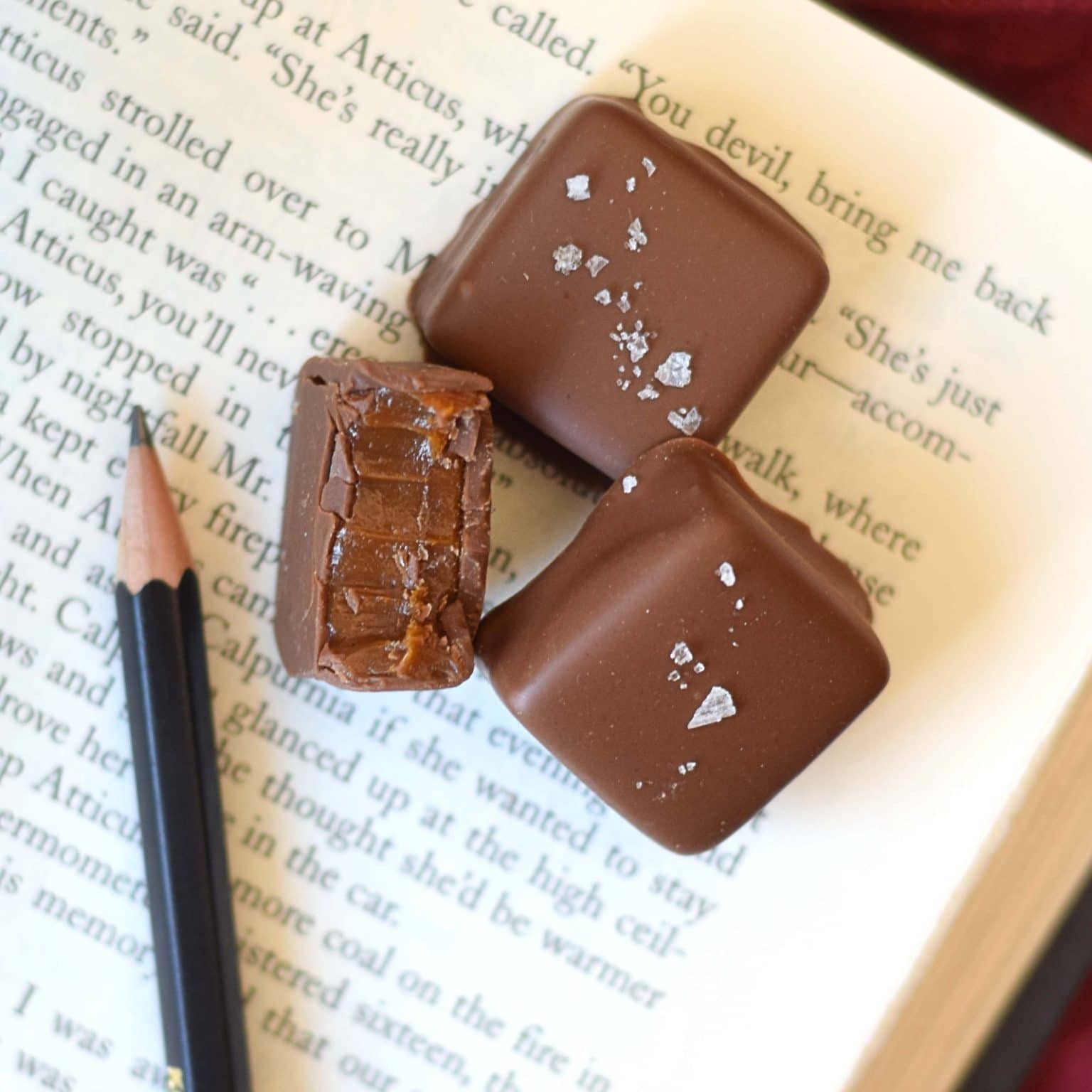 Three gourmet milk chocolate sea salt caramels sitting on an open book. One truffle has a bite taken out of it.
