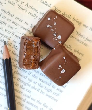 Three gourmet milk chocolate sea salt caramels sitting on an open book. One truffle has a bite taken out of it.