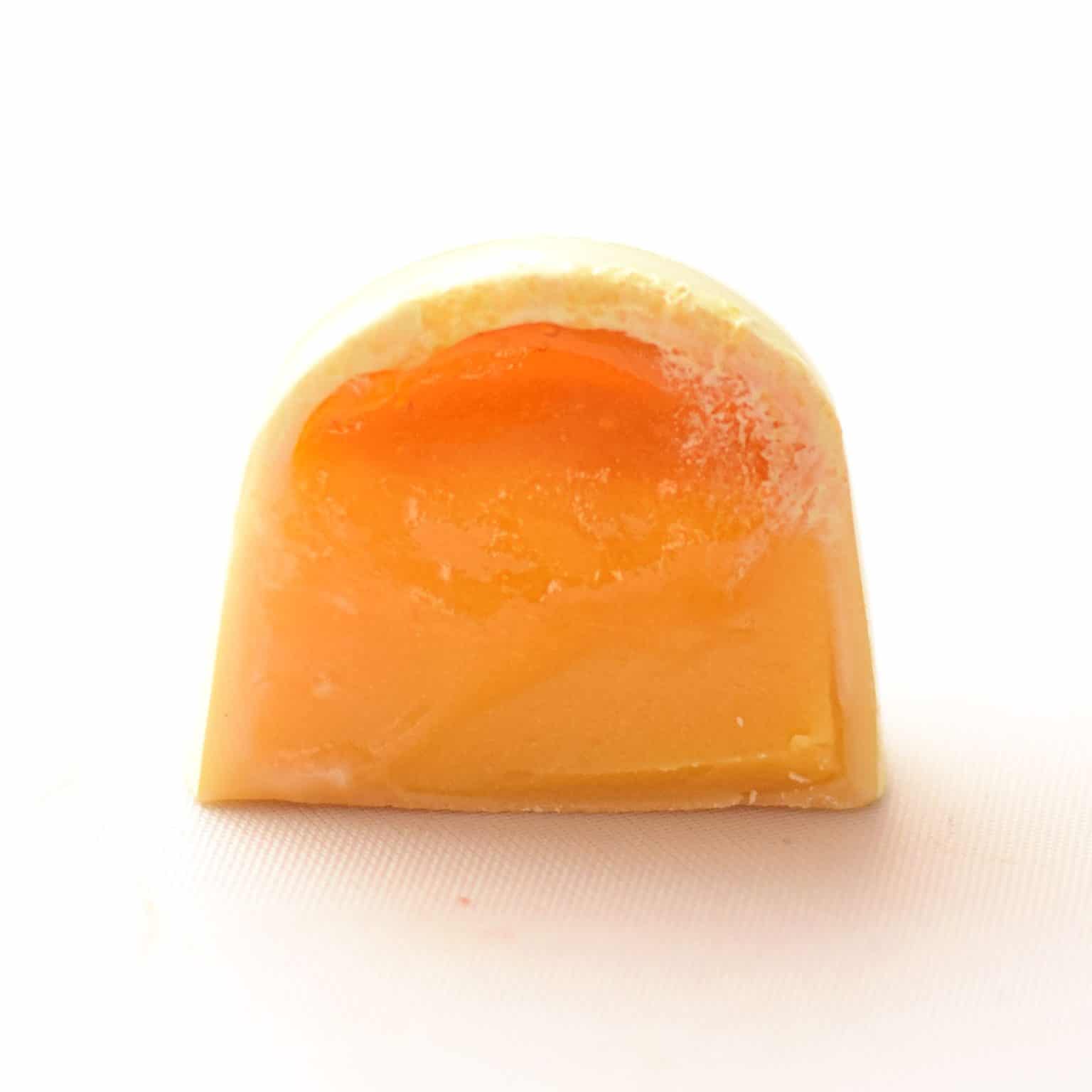 Inside view of a gourmet white chocolate truffle that contains a thick layer of passion fruit ganache and a thin layer of passion fruit jelly