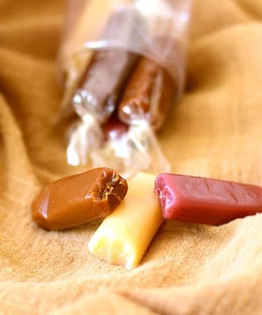 Three different natural-flavored caramels (sea salt caramel, vanilla, raspberry) in the foreground with a package in the background