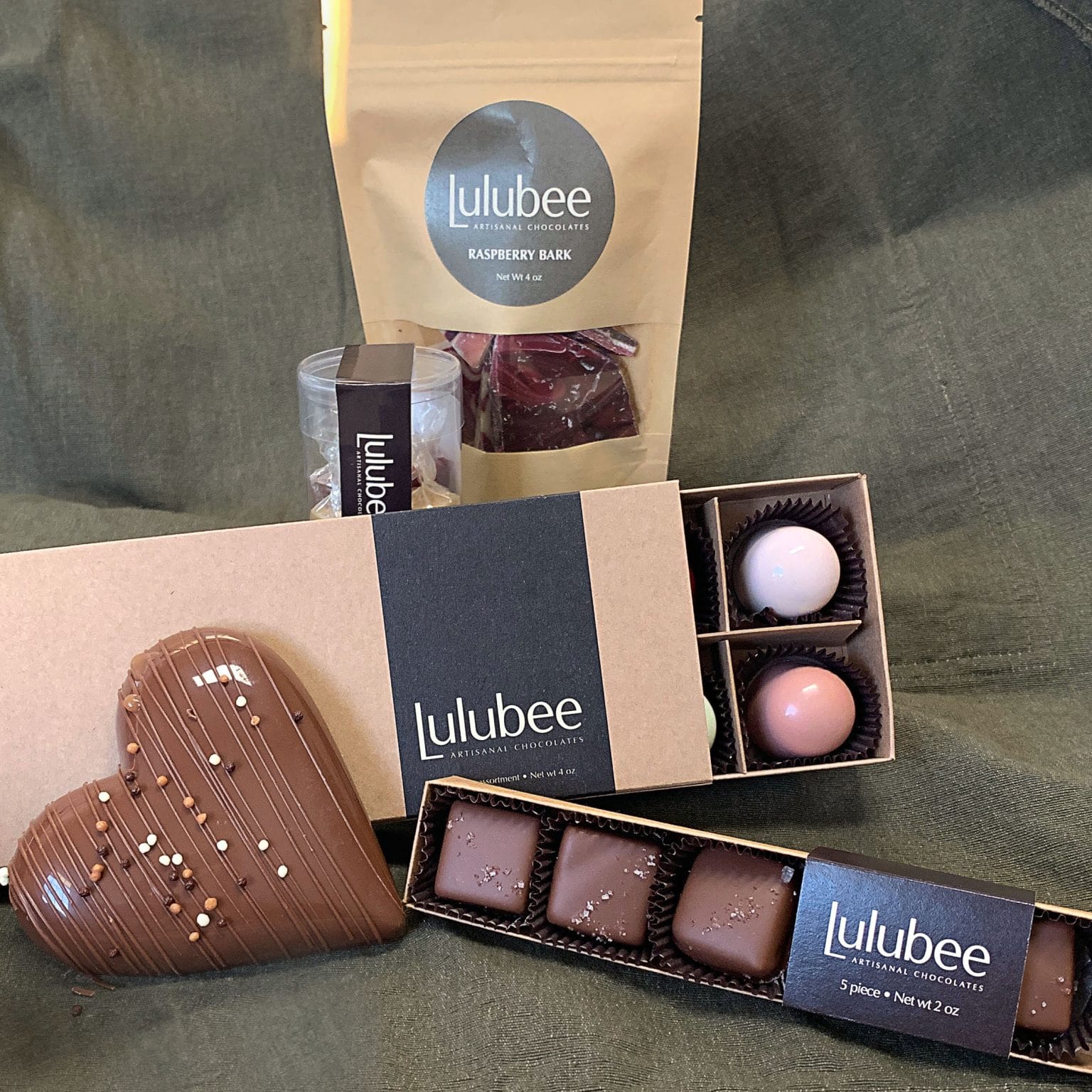 Collection of 5 different packages that contain 12 gourmet chocolate truffles, raspberry chocolate bark, confections, sea salt caramels, and a large gourmet milk chocolate heart