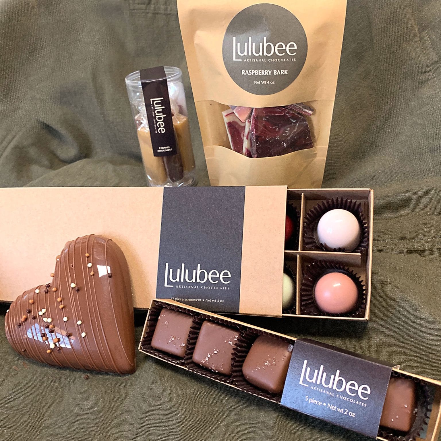 Collection of 5 different packages that contain 12 pastel-colored gourmet chocolate truffles, raspberry chocolate bark, confections, sea salt caramels, and a large gourmet milk chocolate heart