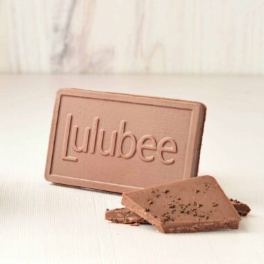Small milk chocolate bar with the Lulubee logo on it; small bits of the chocolate bar are in front of the full bar. The bar is sprinkled with espresso.