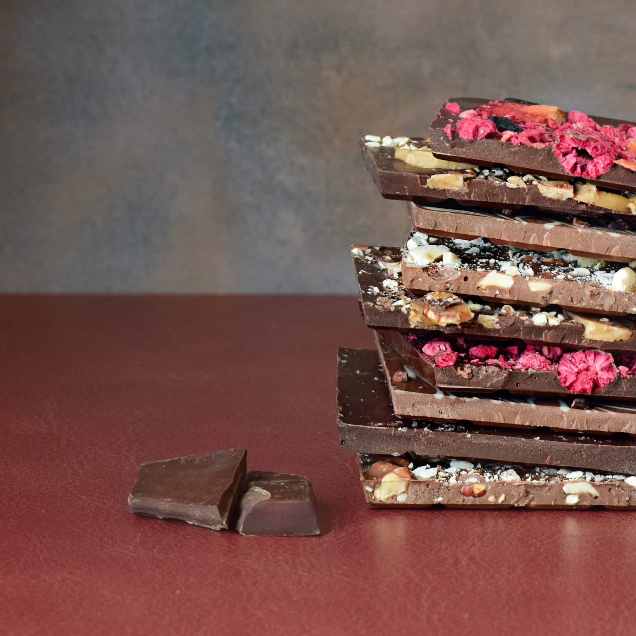 Stack of artisanal chocolate bars in dark, milk, and white chocolates with inclusions in each one.