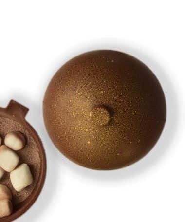 Overhead view of an ornament-shaped Milk Chocolate Cocoa Bomb with an inside view filled with cocoa mix and marshmallows