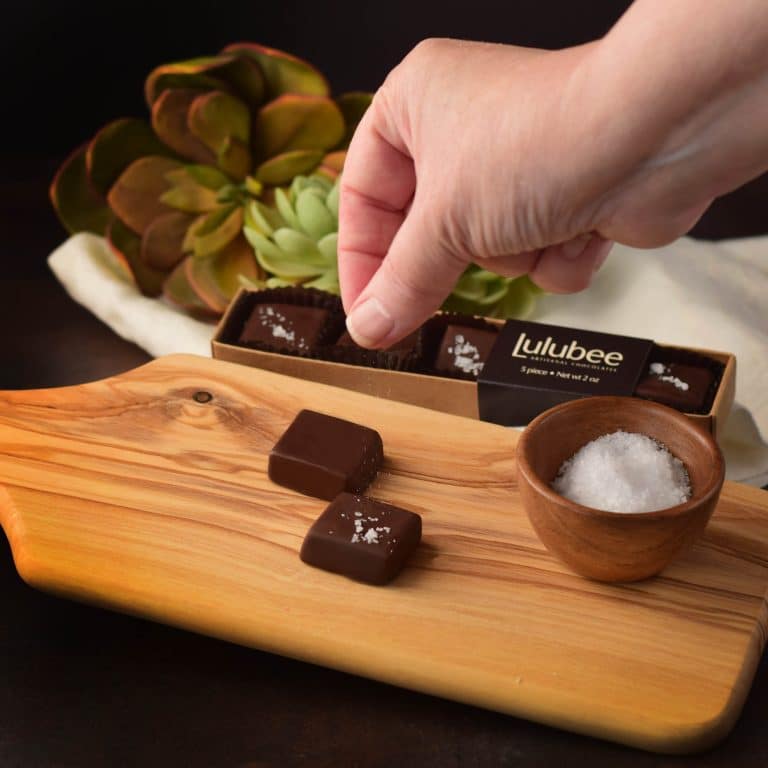Hand sprinkling sea salt on caramels covered in dark chocolate