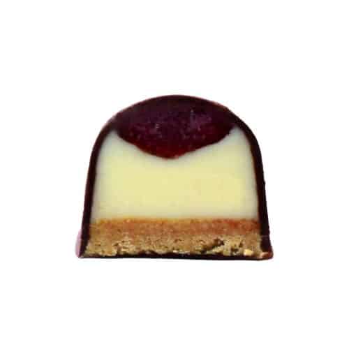 Inside view of a gourmet chocolate bonbon that has three layers: strawberry jelly, cream cheese ganache, and graham cracker