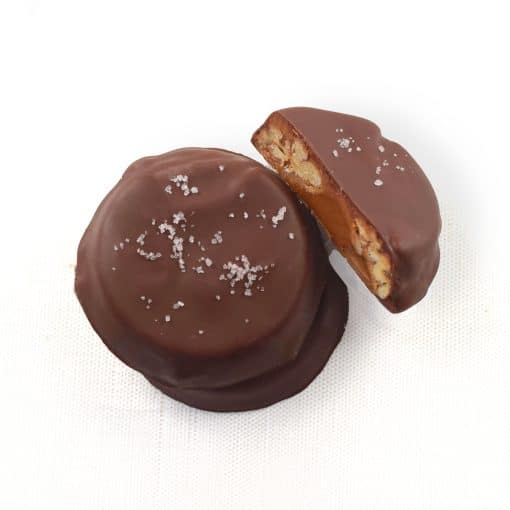 Overhead view of three gourmet Dark Chocolate Pecan Turtles; one turtle is cut in half to reveal the caramel and pecans inside