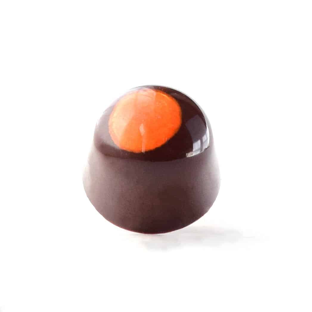 Side view of a dark brown gourmet chocolate truffle with a large orange dot on the top; the truffle tastes like orange and dark chocolate