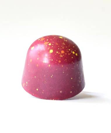 Fall-red gourmet chocolate truffle with orange and yellow dots splattered on it